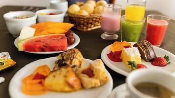 Una mesa de desayuno con diversas frutas, pasteles y bebidas.