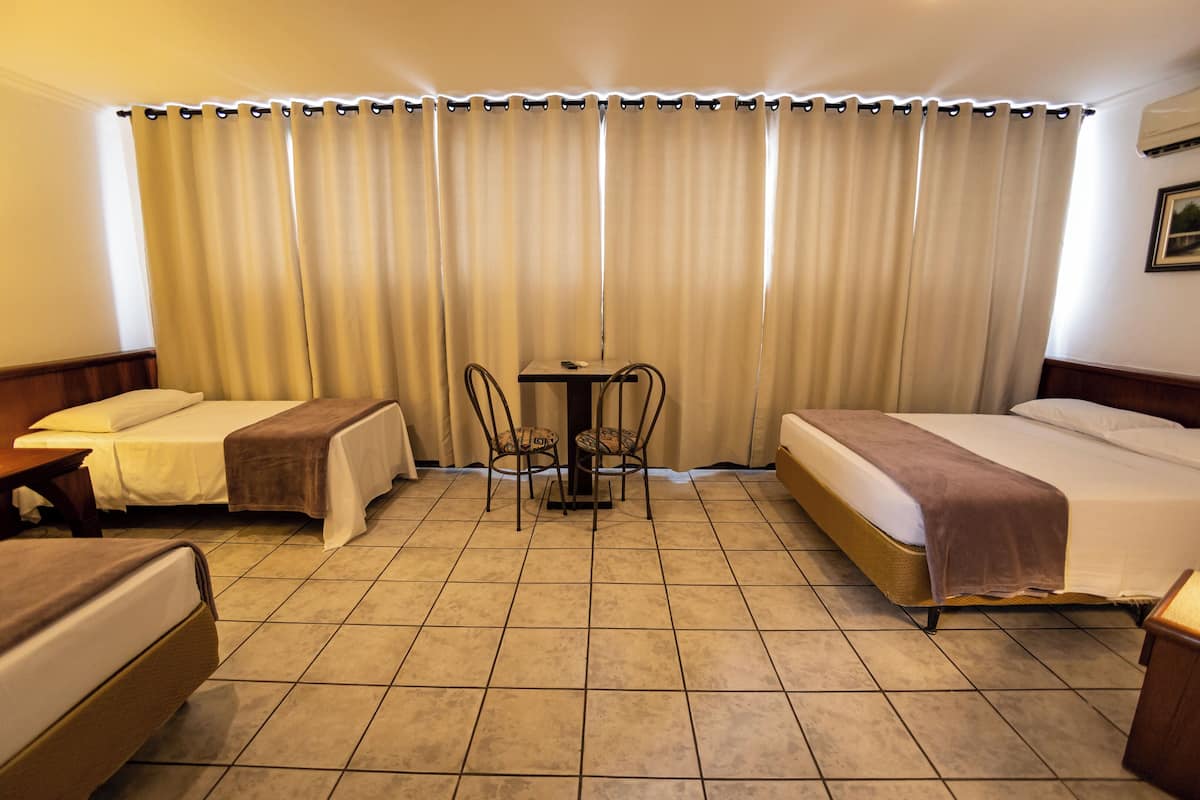 A hotel room with two single beds, a small table with chairs, and a large window with curtains.