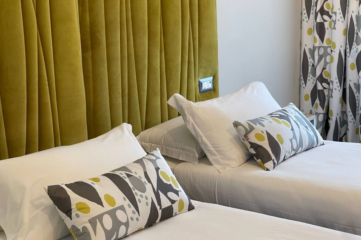 Ein Hotelzimmer mit zwei Betten, jeweils mit weißer Bettwäsche und gemusterten Kissen.
