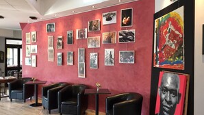 A lobby with a red wall adorned with framed photographs and a large abstract painting. There are black leather chairs and a small table with a vase.