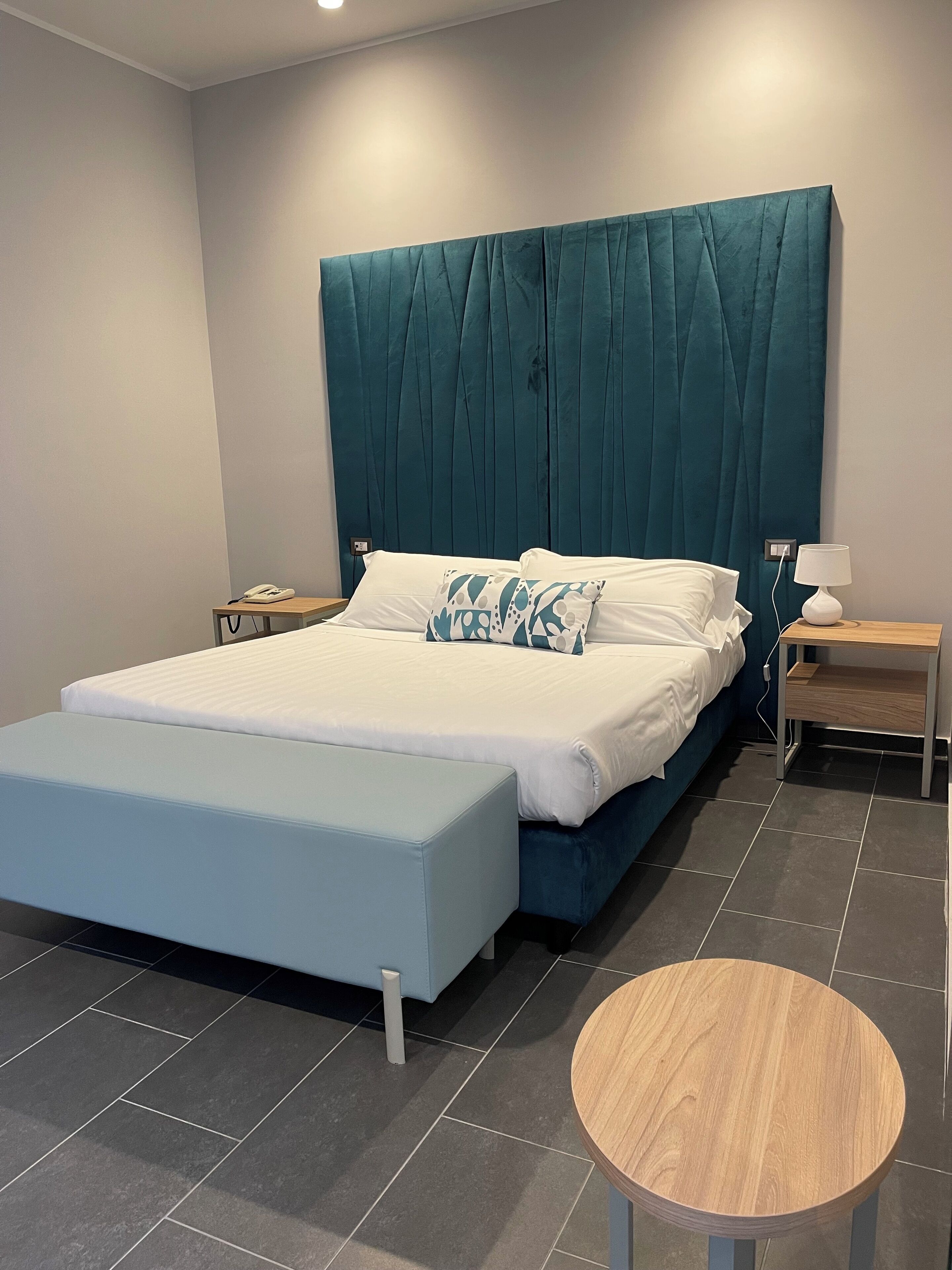 Un dormitorio moderno con una cama grande, una mesita de noche con lámpara y una pequeña mesa redonda.