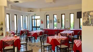 A dining area with multiple tables covered in red tablecloths, arranged in rows with chairs.