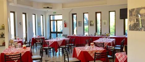 A dining area with multiple tables covered in red tablecloths, arranged in rows with chairs.