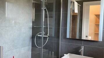 Een moderne badkamer met een douchecabine van glas, een witte wastafel en een grote spiegel.
