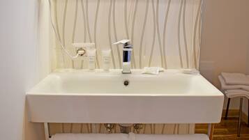 Un baño con lavamanos blanco, espejo y toallero.