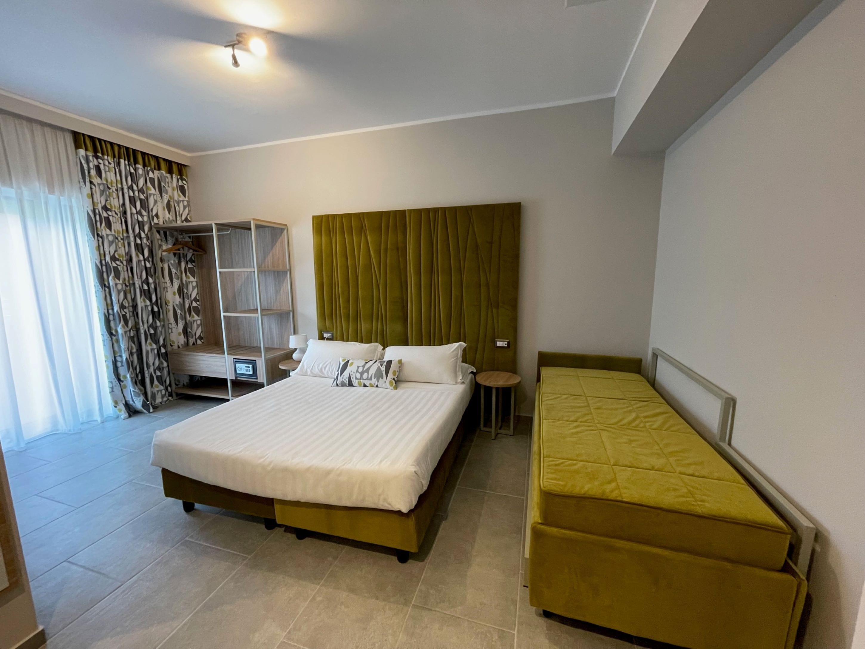 A hotel room with a large bed, a smaller bed, a wardrobe, and a seating area.