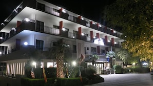 A multi-story hotel with balconies, a well-lit entrance, and a landscaped garden area.
