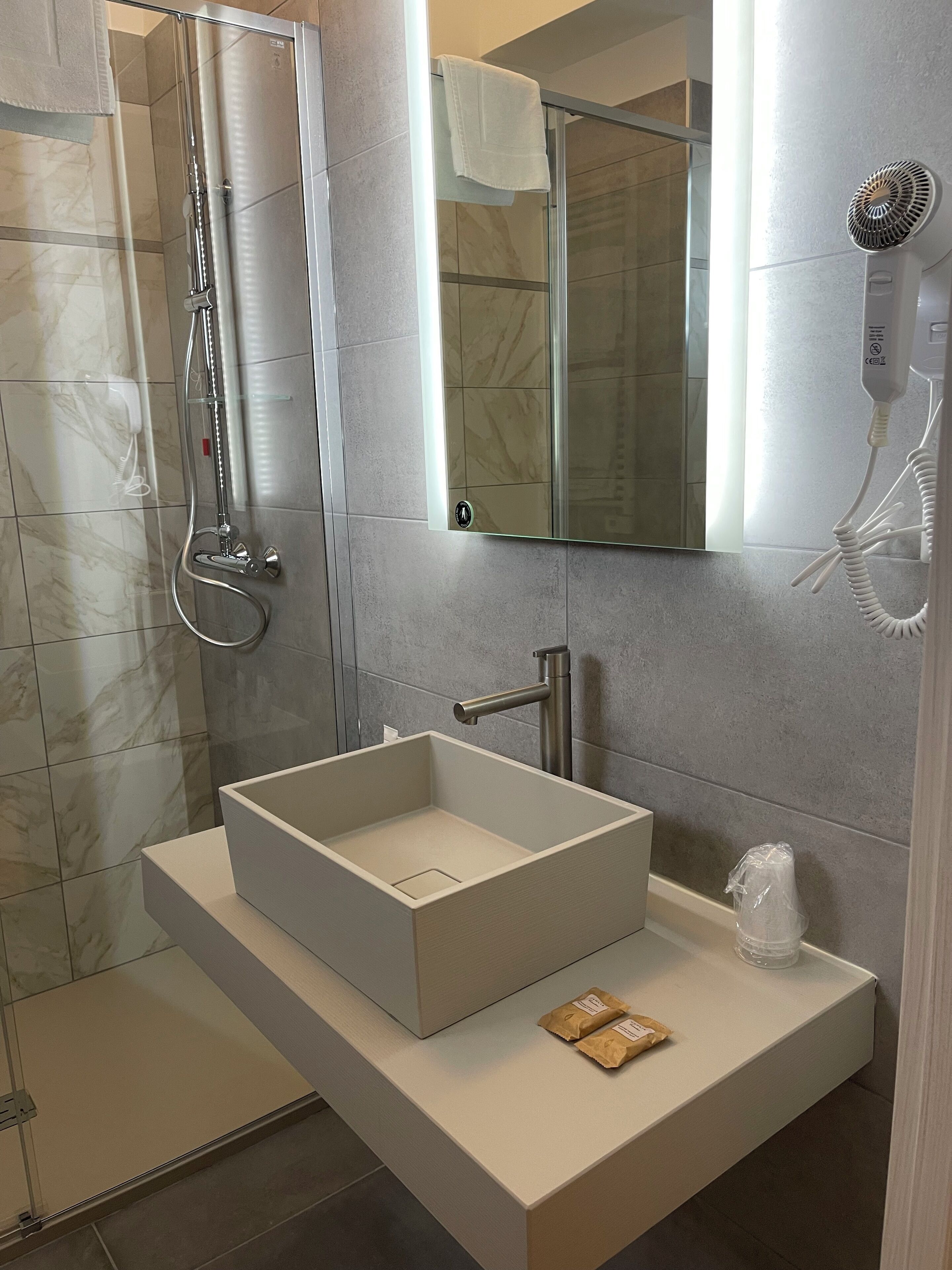 A modern bathroom with a glass-enclosed shower, a large mirror, and a built-in sink with a towel rack.