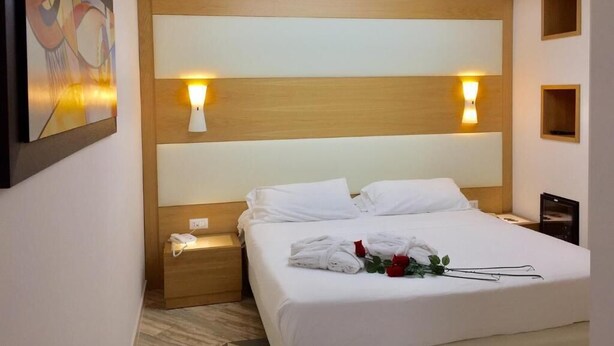 A hotel room with a large bed, two bedside lamps, a painting on the wall, and a skylight above.