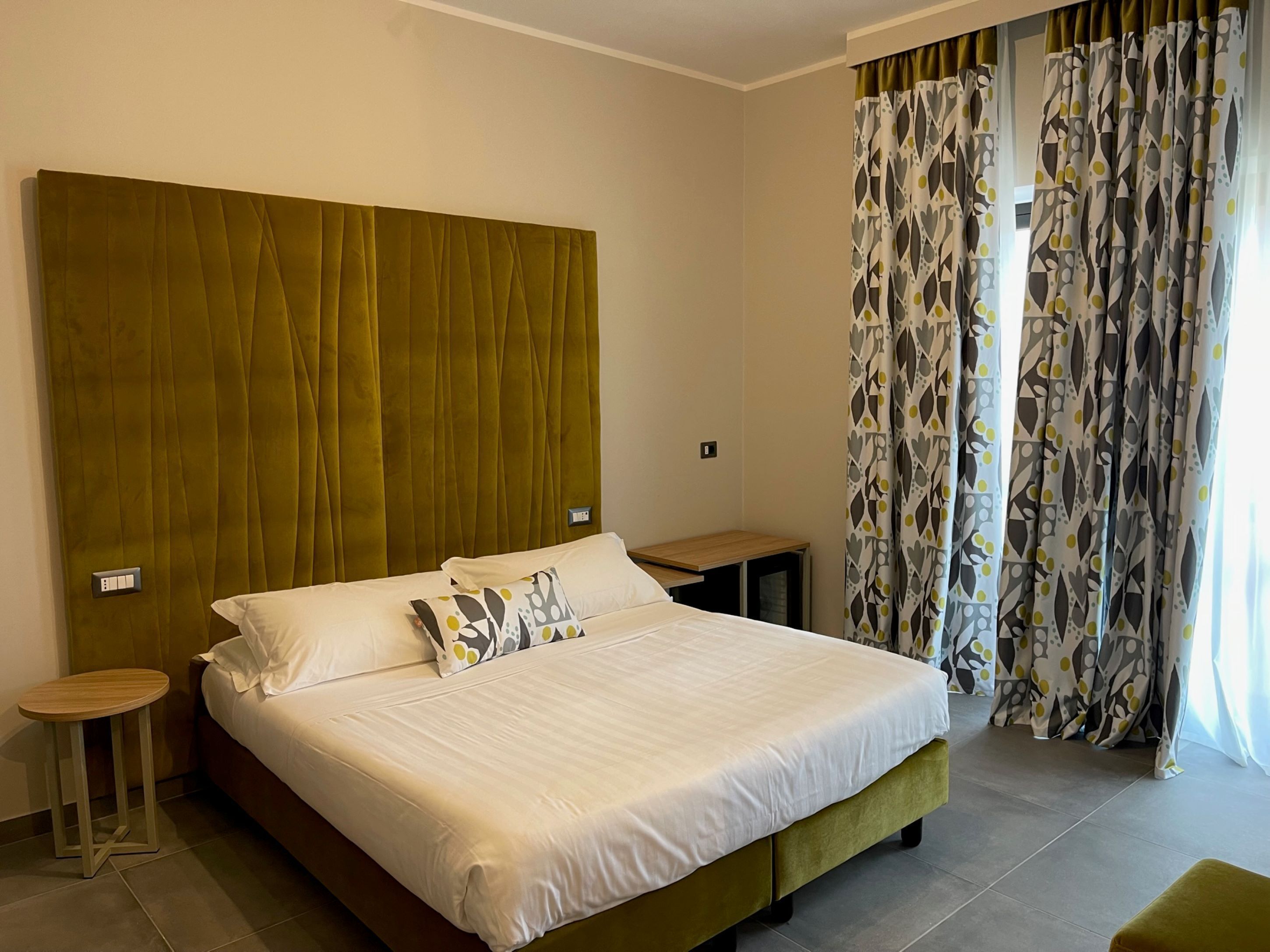 Una habitación de hotel con una cama grande, una mesita de noche y una ventana con cortinas estampadas.