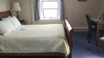 Une chambre à coucher avec un lit, une table de chevet avec une lampe, une fenêtre avec des rideaux, un bureau avec une chaise et un tableau encadré au mur.