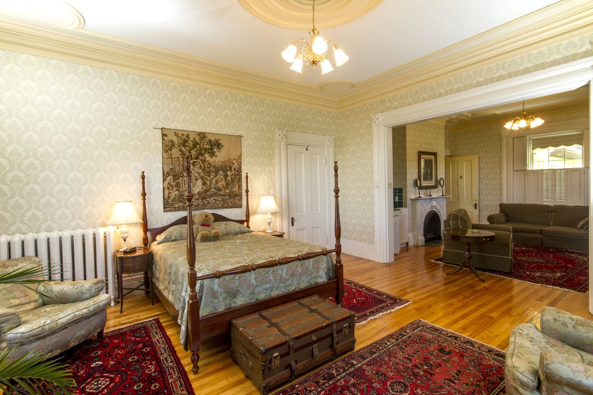 Une chambre spacieuse avec un lit à baldaquin, un coin salon avec un canapé et des fauteuils, et un coin repas avec une cheminée.