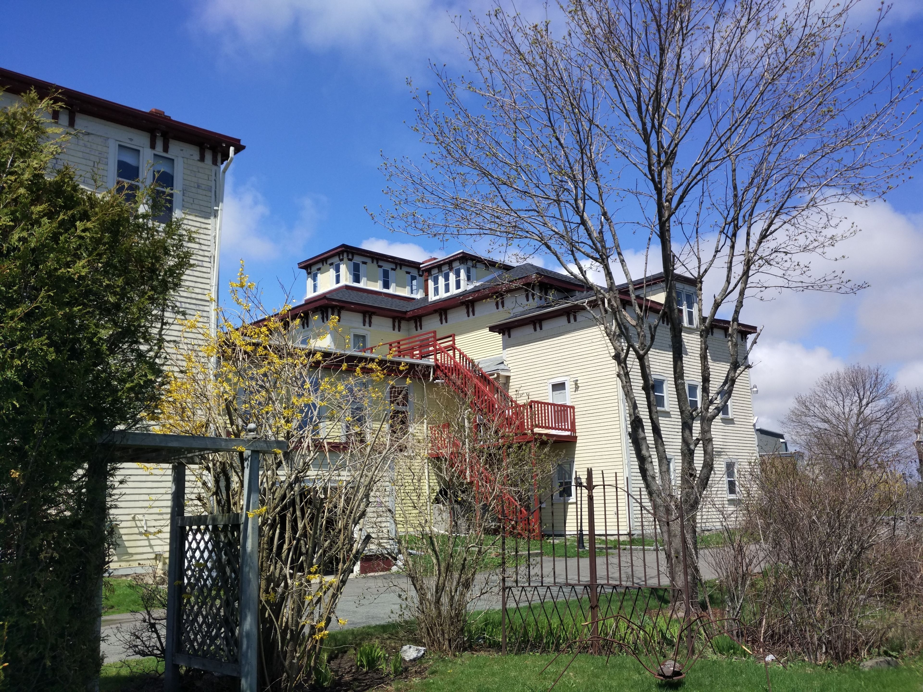 A multi-story building with a red staircase, a fenced garden, and a clear blue sky.