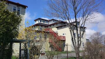 A multi-story building with a red staircase, a fenced garden, and a clear blue sky.