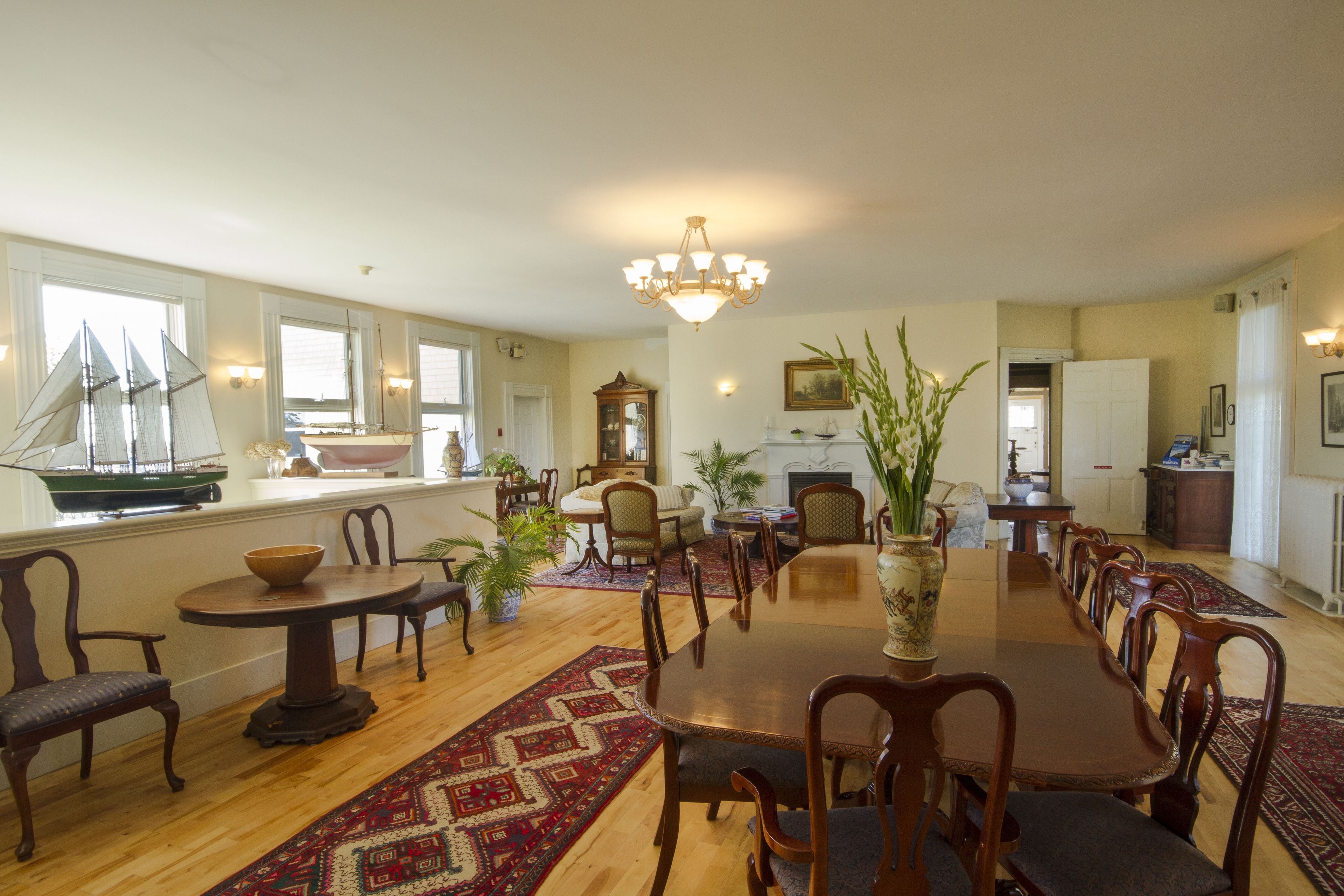 A spacious dining area with a large wooden table and chairs, surrounded by potted plants and a decorative rug.