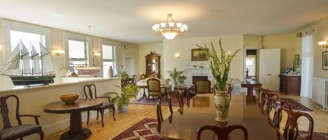 A spacious dining area with a large wooden table and chairs, surrounded by potted plants and a decorative rug.