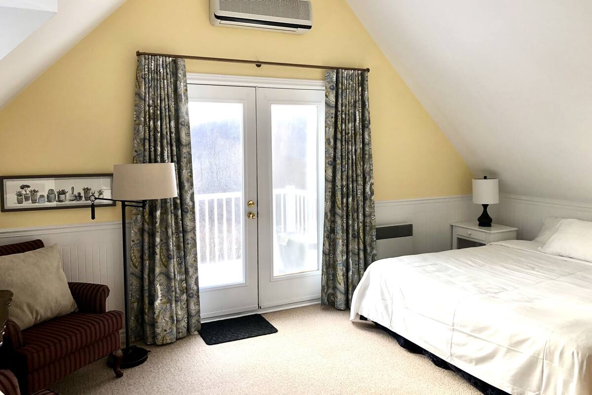 A bedroom with a bed, a nightstand, a lamp, a window with curtains, and a picture on the wall.