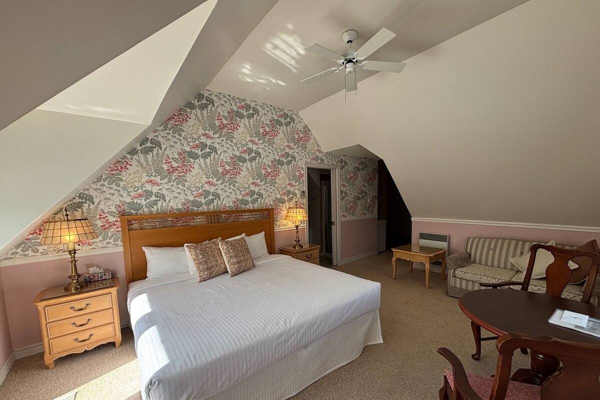 A bedroom with a bed, a desk, a chair, a ceiling fan, and a door.