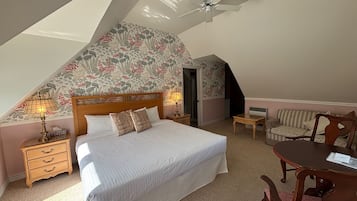 A bedroom with a bed, a desk, a chair, a ceiling fan, and a door.