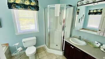 A bathroom with a toilet, shower, sink, and a window with a floral curtain.