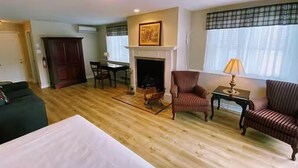 A hotel room with a fireplace, a dining area, a sofa, and a bed. - Auberge Le Tricorne (Hatley)