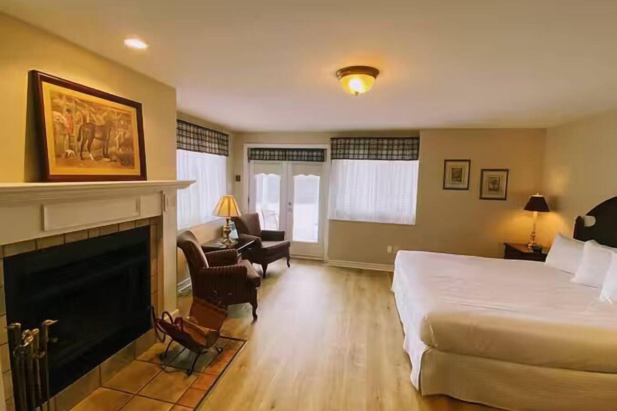 A hotel room with a fireplace, a bed, a desk with a chair, and a window with curtains.