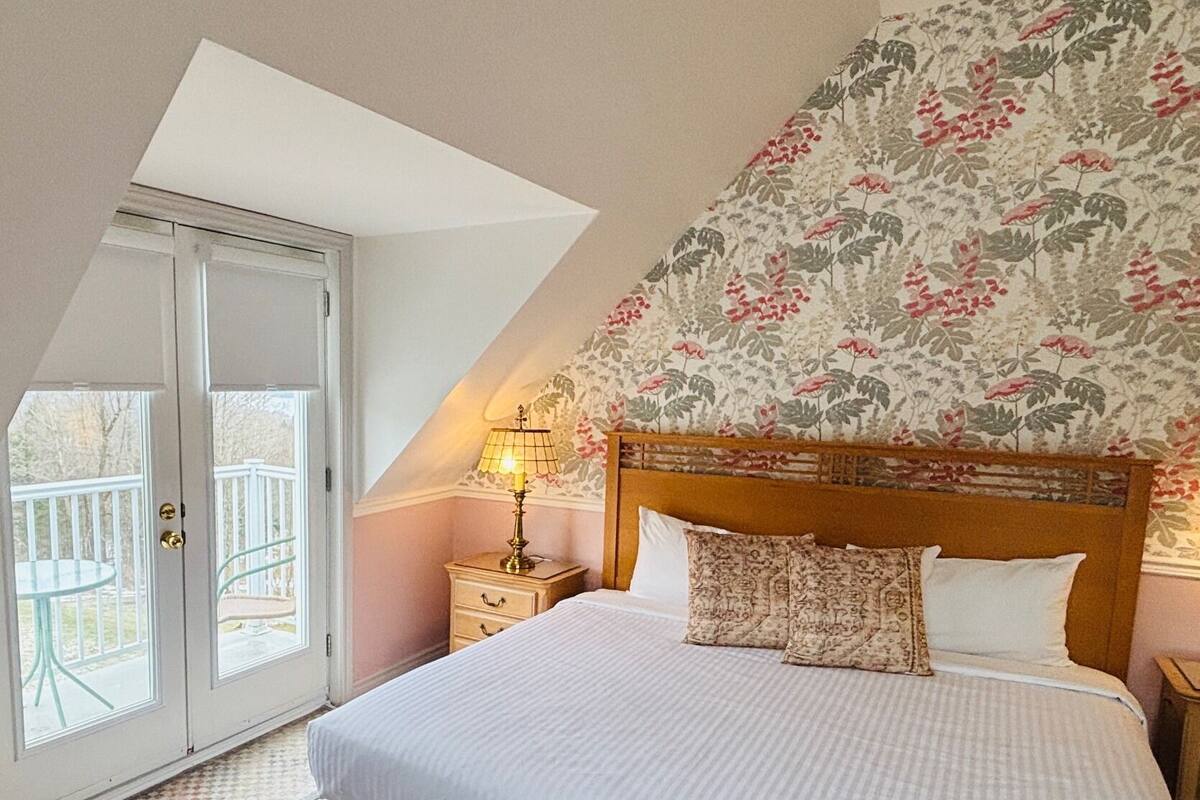 A bedroom with a bed, a nightstand, a lamp, a dresser, and a balcony.