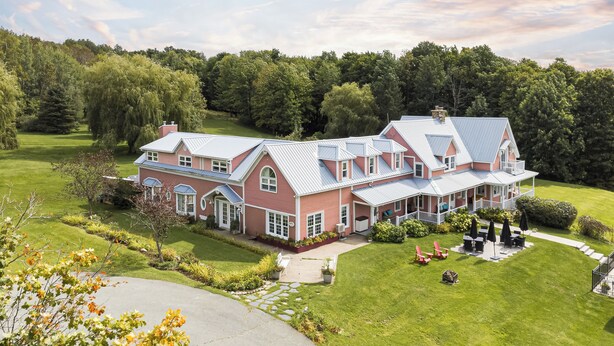 A large, two-story house with a red brick exterior and a grey roof, surrounded by a well-maintained lawn and trees. - Auberge Le Tricorne (Hatley)