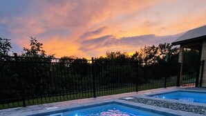 A swimming pool with clear water, surrounded by a black fence and a building in the background. - Auberge Le Tricorne (Hatley)