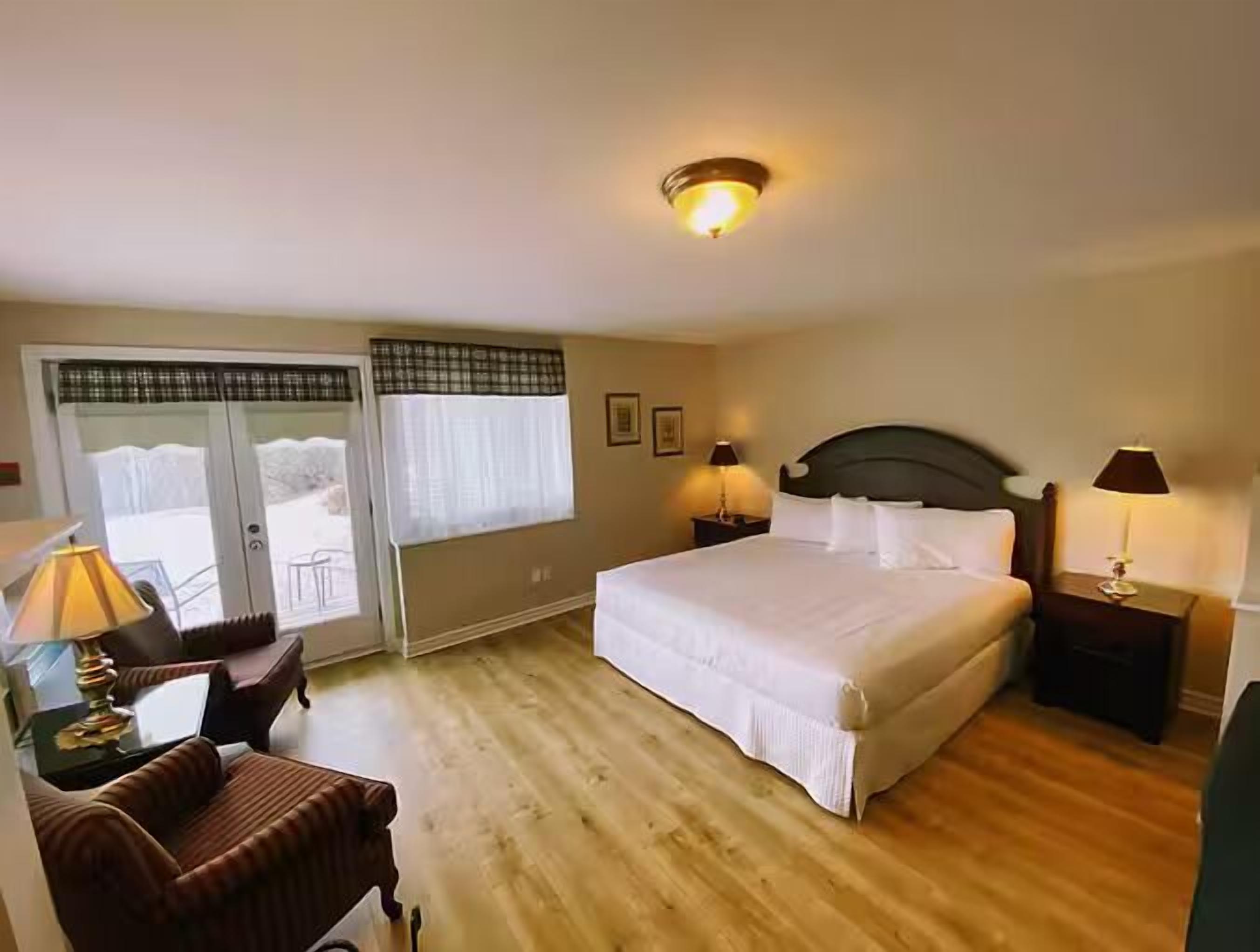 A hotel room with a large bed, two bedside tables with lamps, a chair, a sliding glass door leading to a balcony, and a ceiling light fixture.