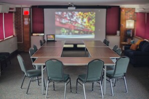 A conference room with a long table, six chairs, a projector screen, and a brick wall. - The Inn At Crumpin Fox (Bernardston)