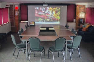 Un salón de conferencias con una larga mesa, seis sillas, una pantalla de proyector y una pared de ladrillo.