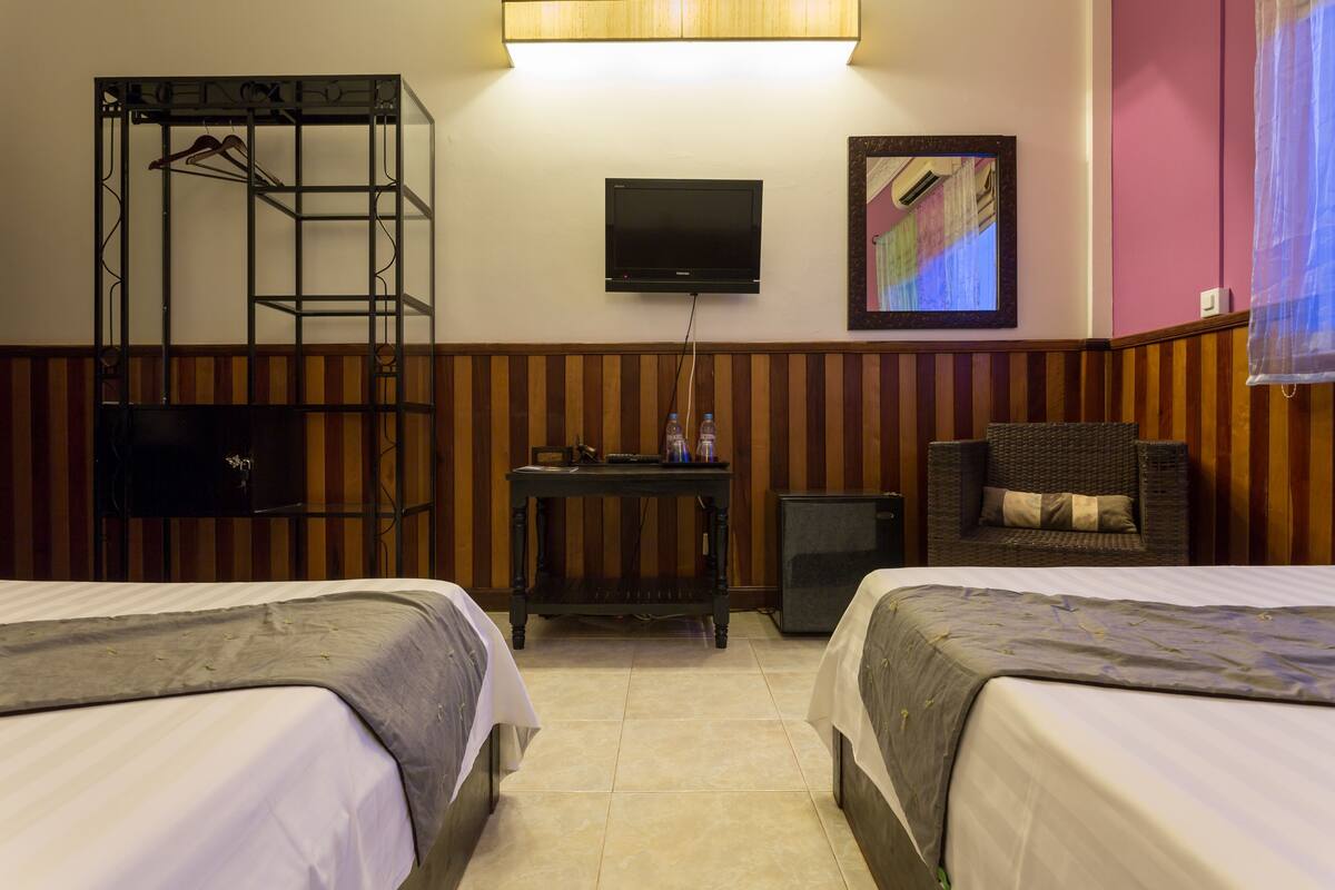 A hotel room with two beds, a TV, a desk with a chair, and a wardrobe.