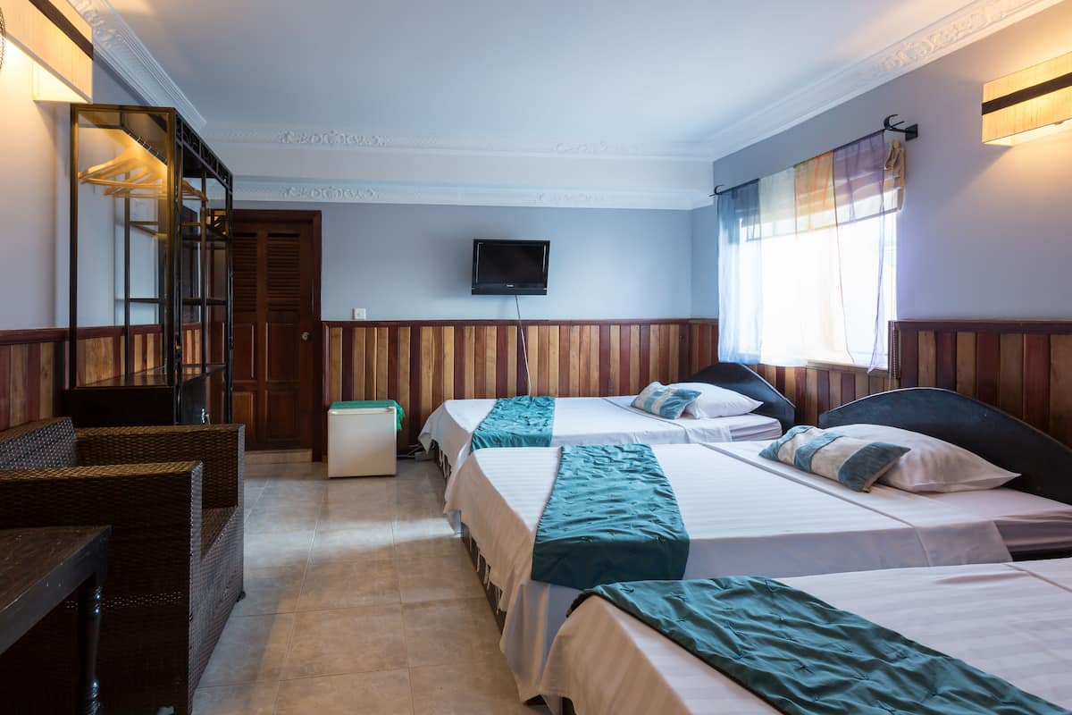 A hotel room with two beds, a television on the wall, a wooden bench, and a window with curtains.