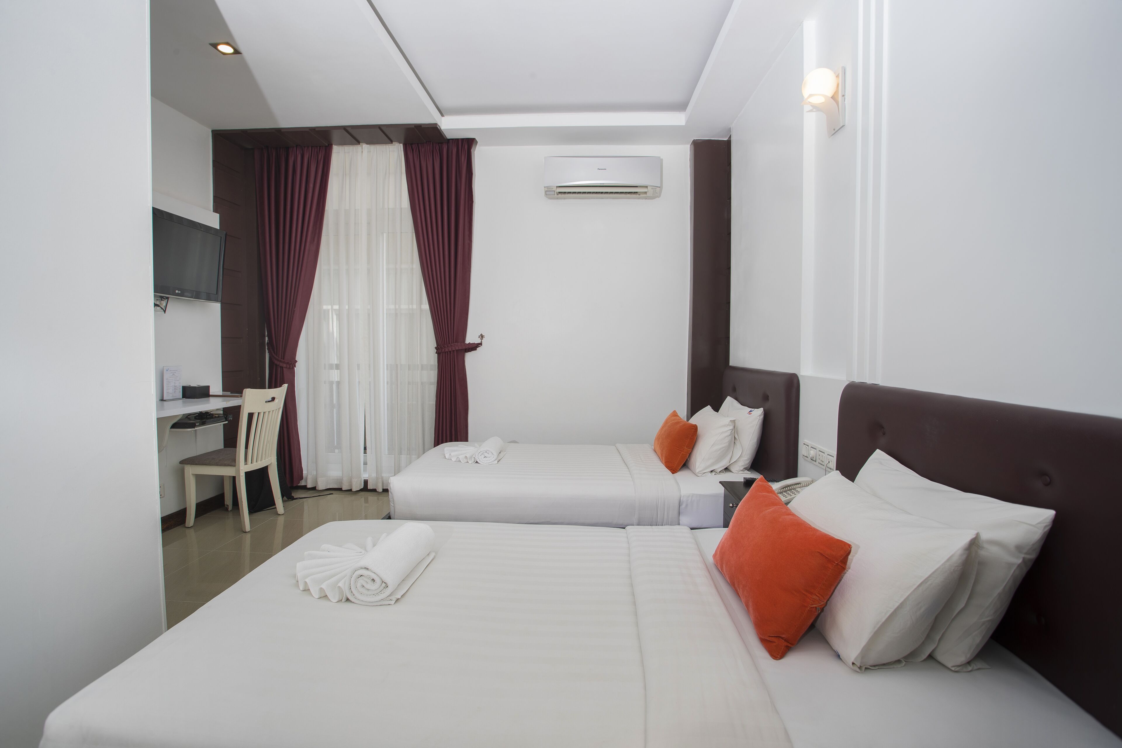 A hotel room with two beds, a desk, and a TV.