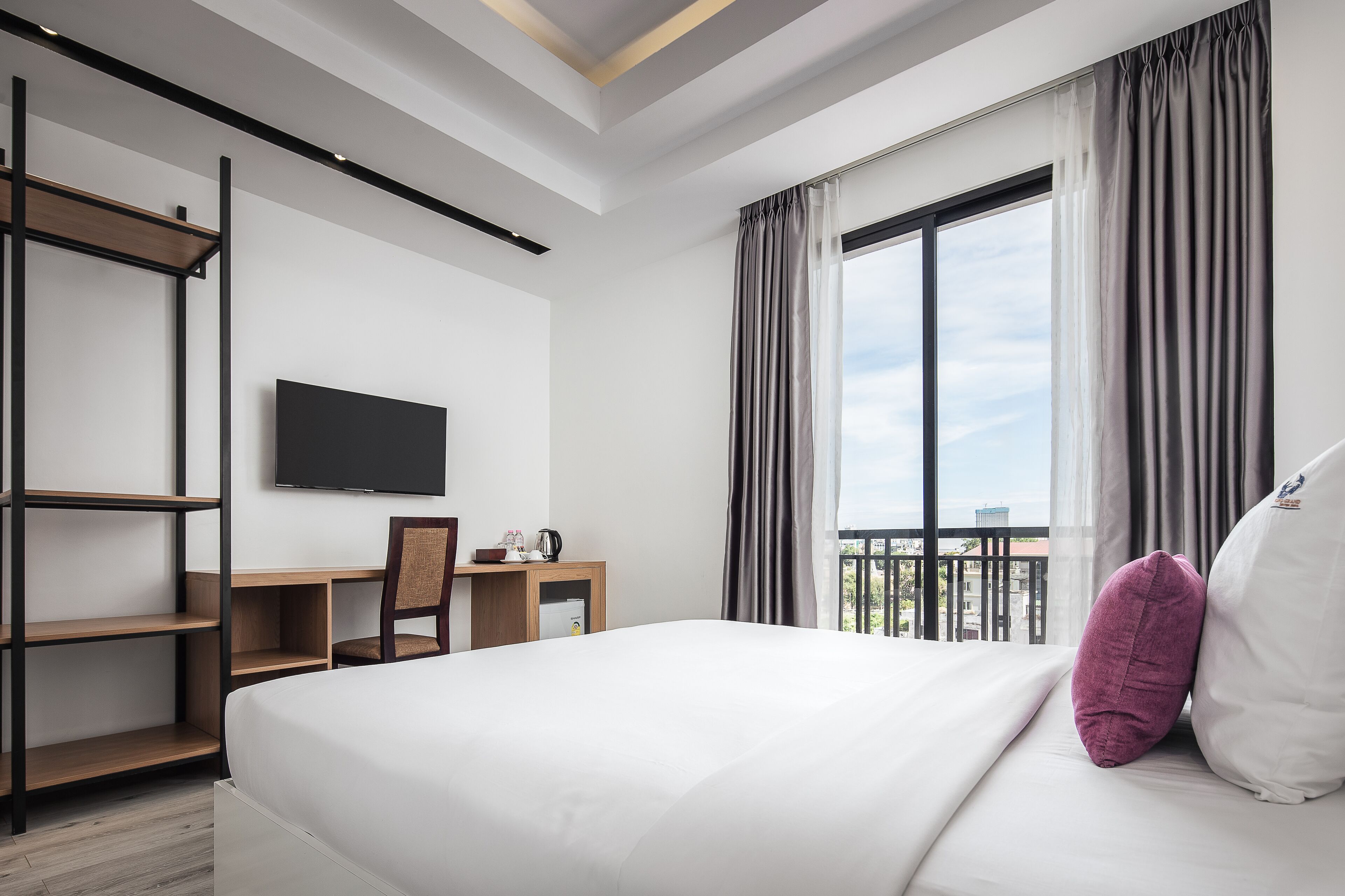 Quarto de hotel com cama, escrivaninha, cadeira, televisão e vista para a varanda.