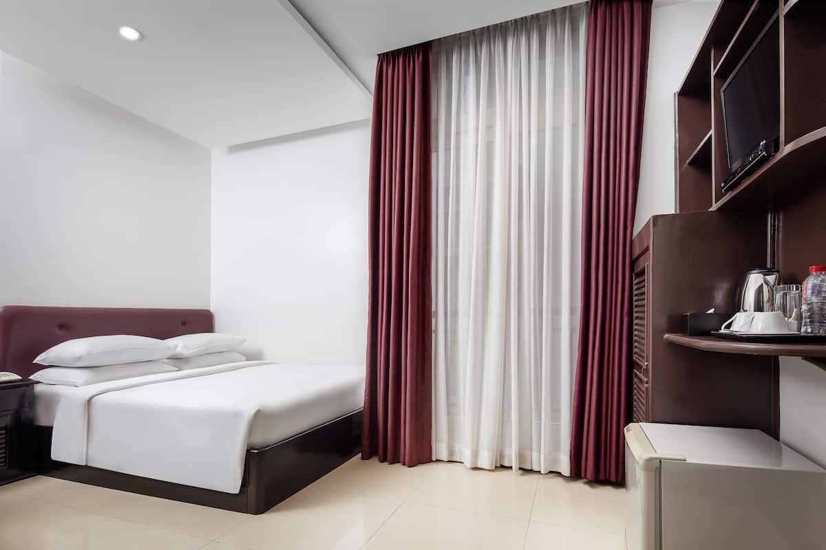Een moderne hotelkamer met een bed, nachtkastje, televisie en een minibar.