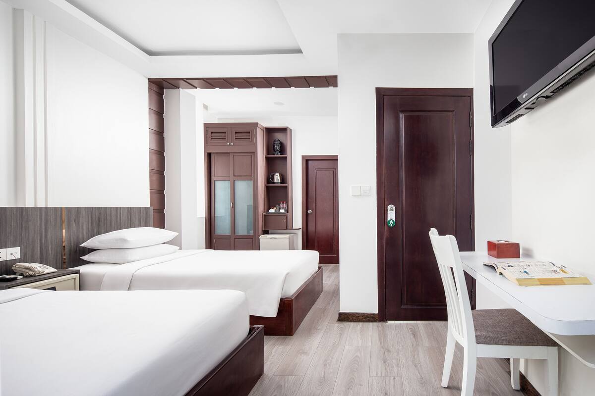Een hotelkamer met twee bedden, een bureau, een televisie en een kledingkast.