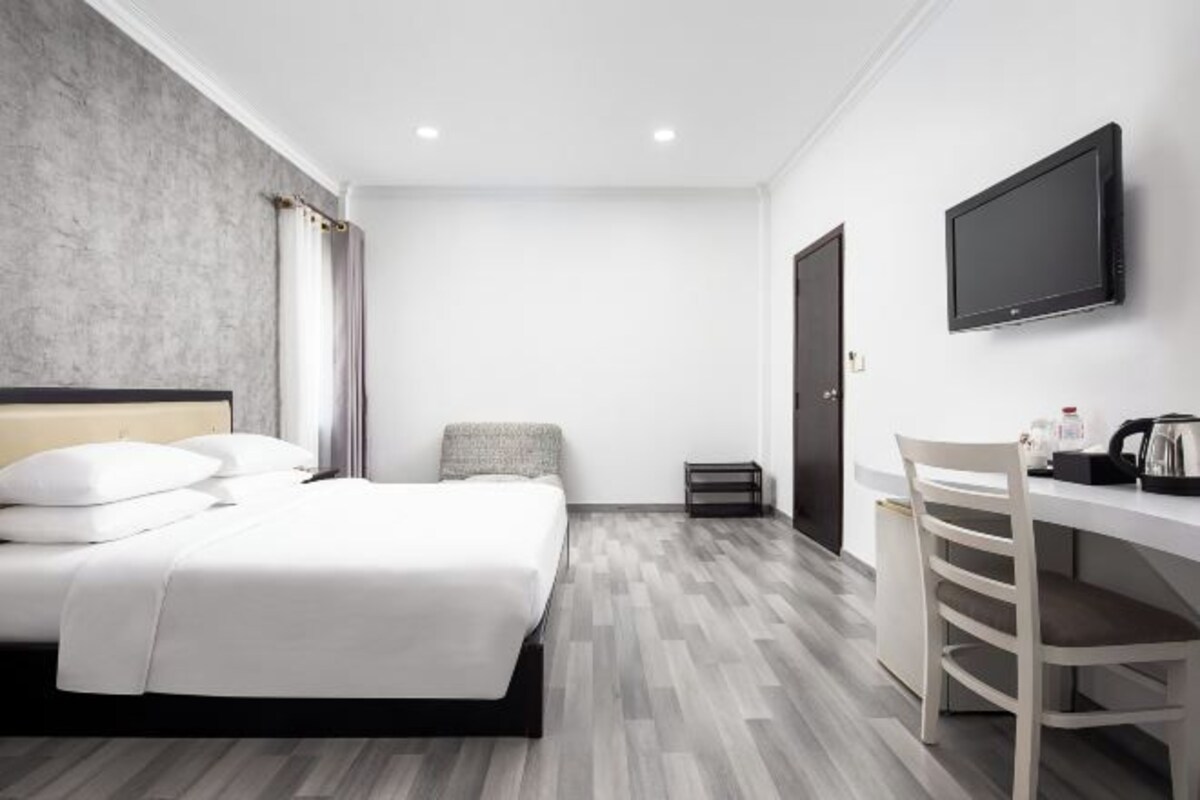 Una habitación de hotel moderna con una cama, un escritorio, una silla, un televisor y un armario.