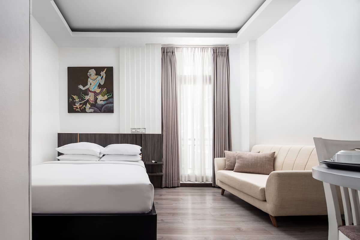 Een moderne hotelkamer met een bed, een slaapbank, een bureau en een groot raam met gordijnen.