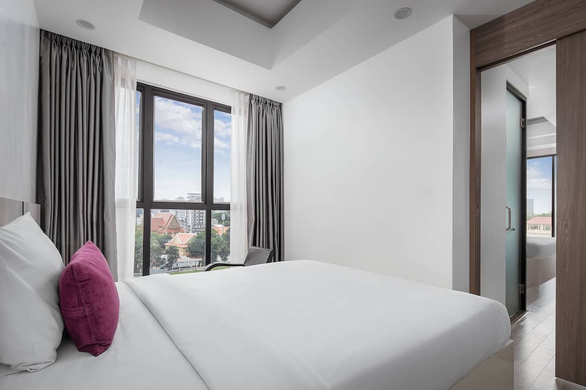 Een hotelkamer met een groot bed, uitzicht op gebouwen en een deur naar een balkon.
