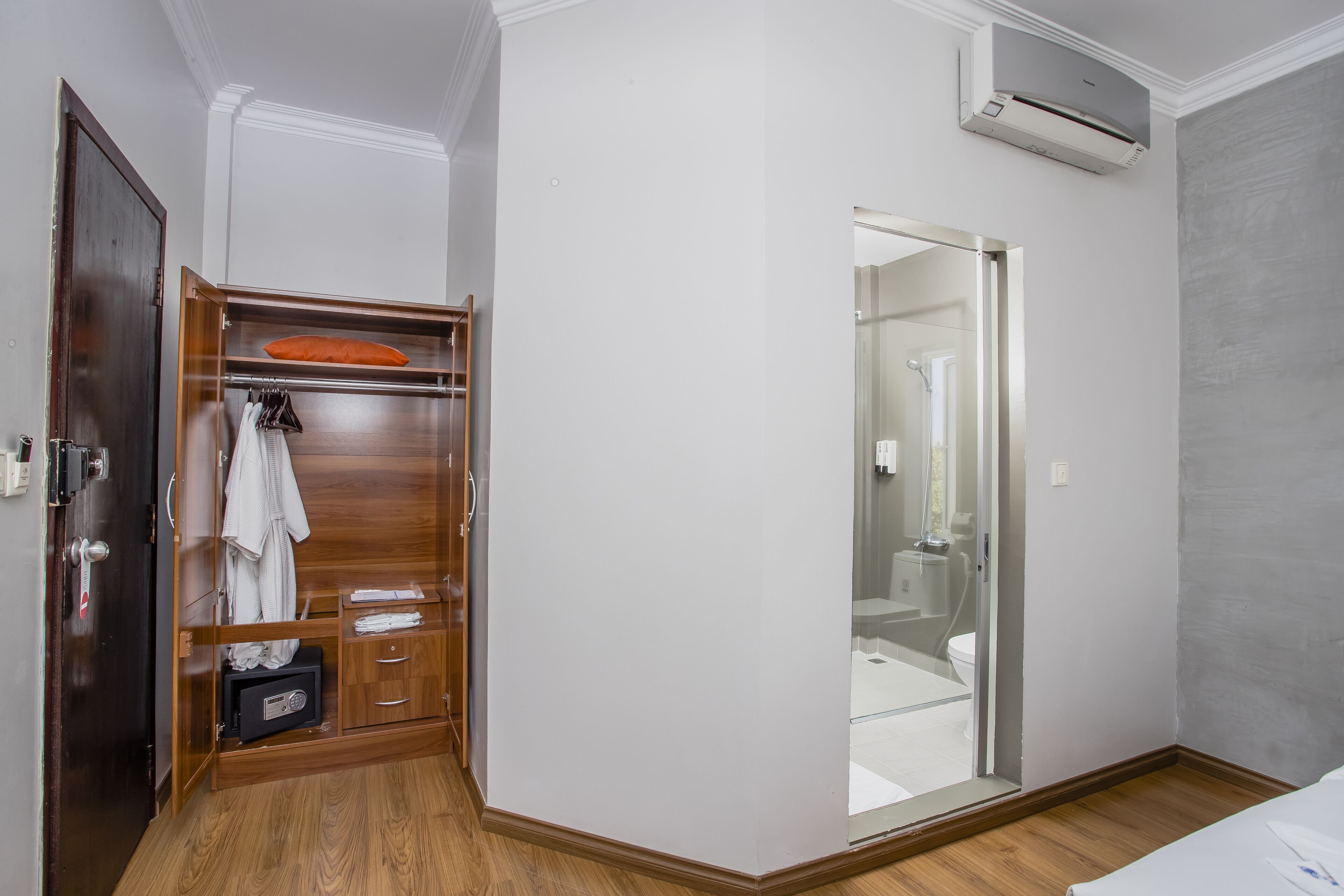 Habitación de hotel con un armario de madera, un espejo y un baño visible a través de una puerta de cristal.