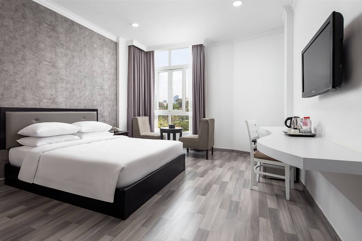 Een moderne hotelkamer met een groot bed, een bureau, een stoel, een televisie en een raam met gordijnen.