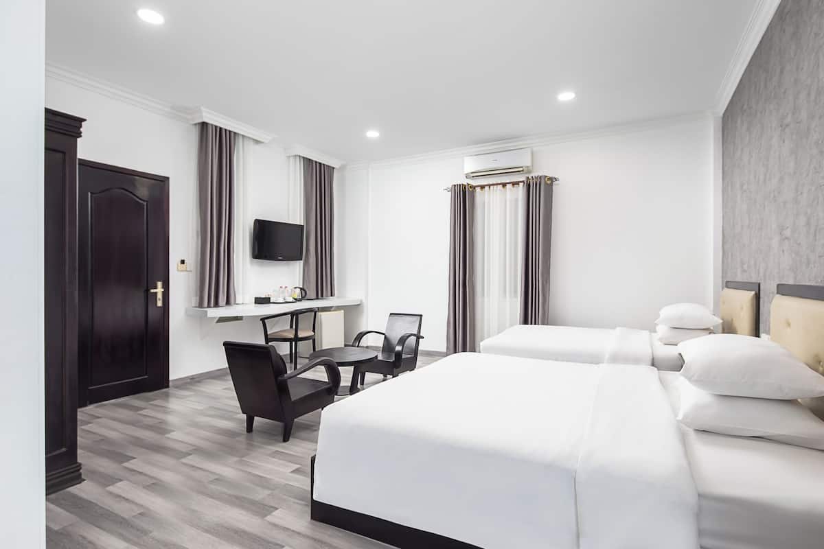 Een hotelkamer met twee bedden, een bureau, een stoel, een televisie en een airconditioning.