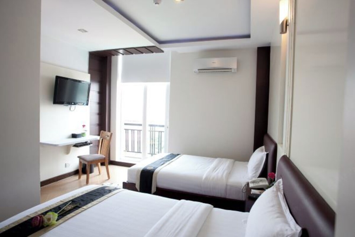 Habitación de hotel con dos camas, un televisor montado en la pared, una silla y un equipo de aire acondicionado.
