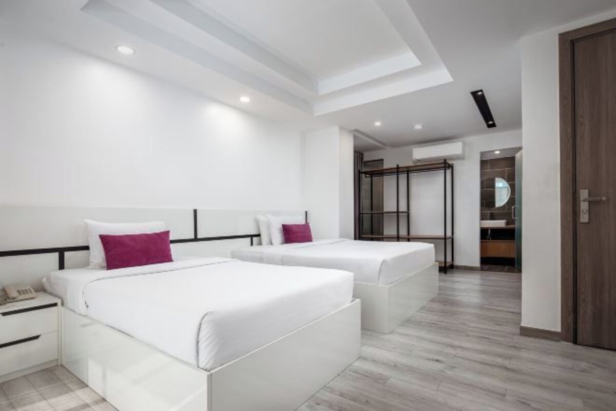 Una habitación de hotel moderna con dos camas, un vestidor y un baño visible a través de una puerta abierta.