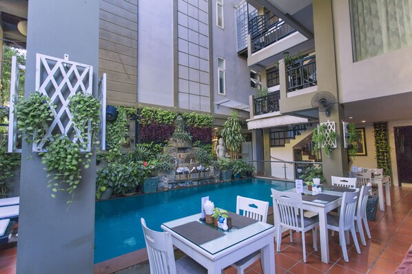 An indoor pool area with a dining setup and multiple levels of balconies. - King Grand Boutique Hotel (Phnom Penh)
