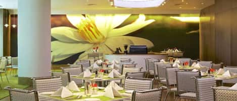 A modern restaurant with round tables and cushioned chairs, a large floral mural on the wall, and a bar area.