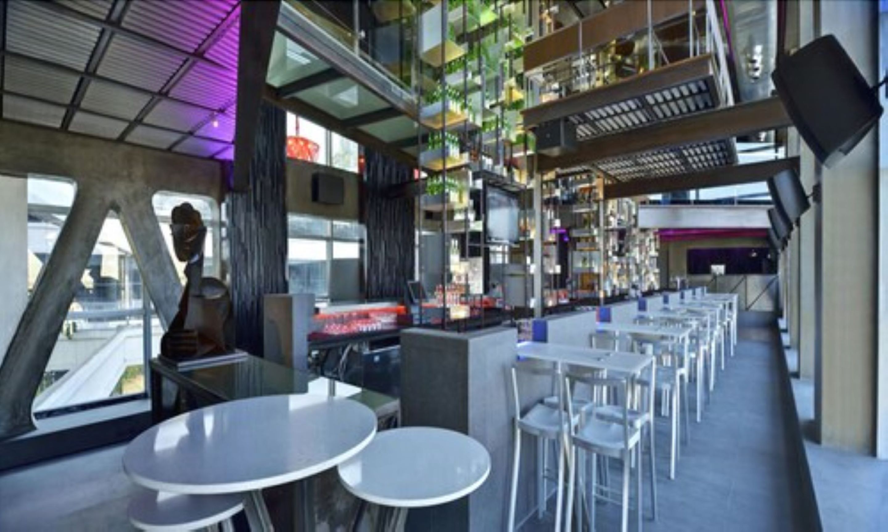 Un restaurante moderno con techos altos, elementos estructurales a la vista y una variedad de opciones de asientos, incluyendo mesas redondas y taburetes de bar.