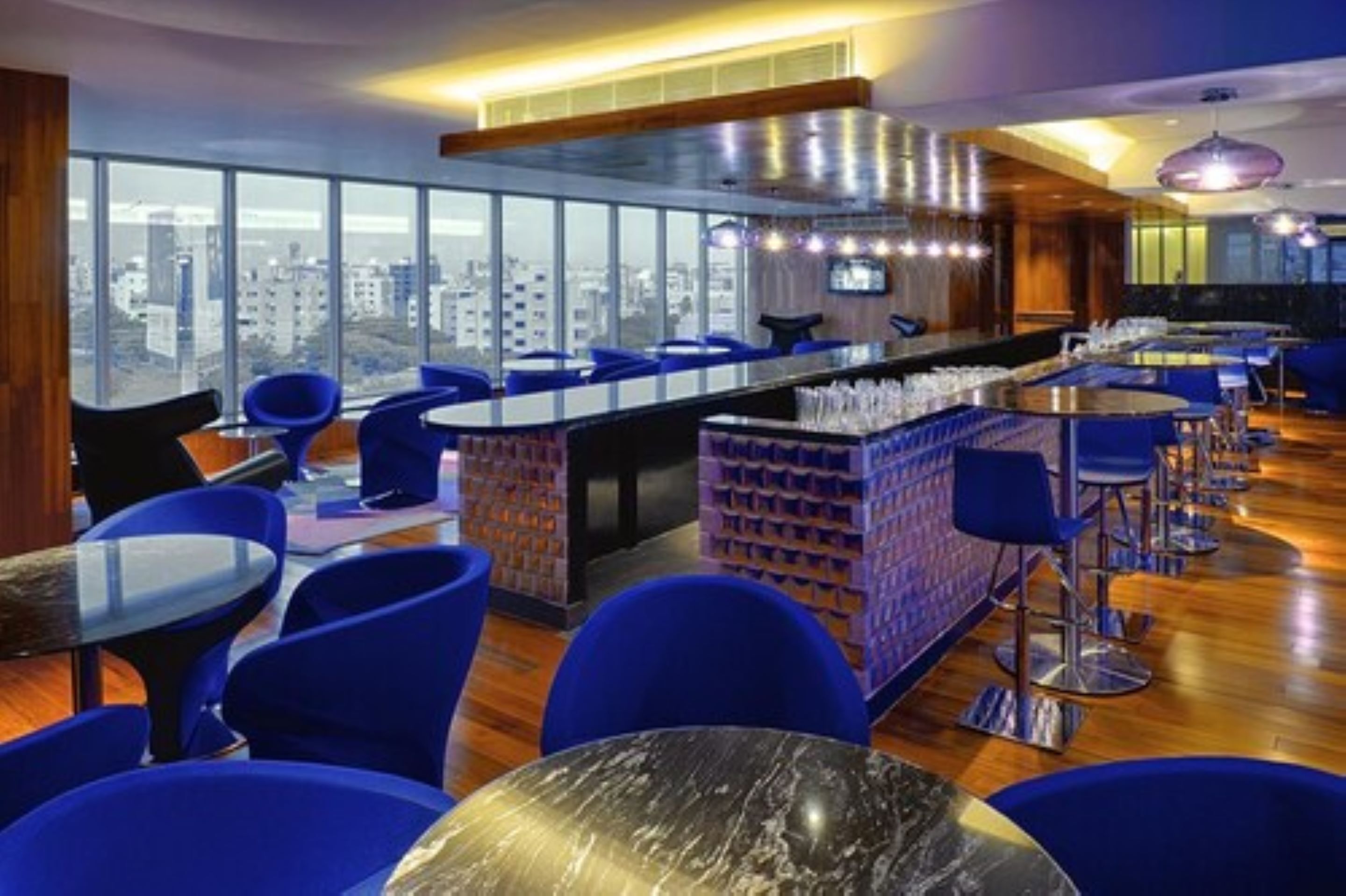 A modern bar area with blue chairs and a marble table, large windows offering a city view.